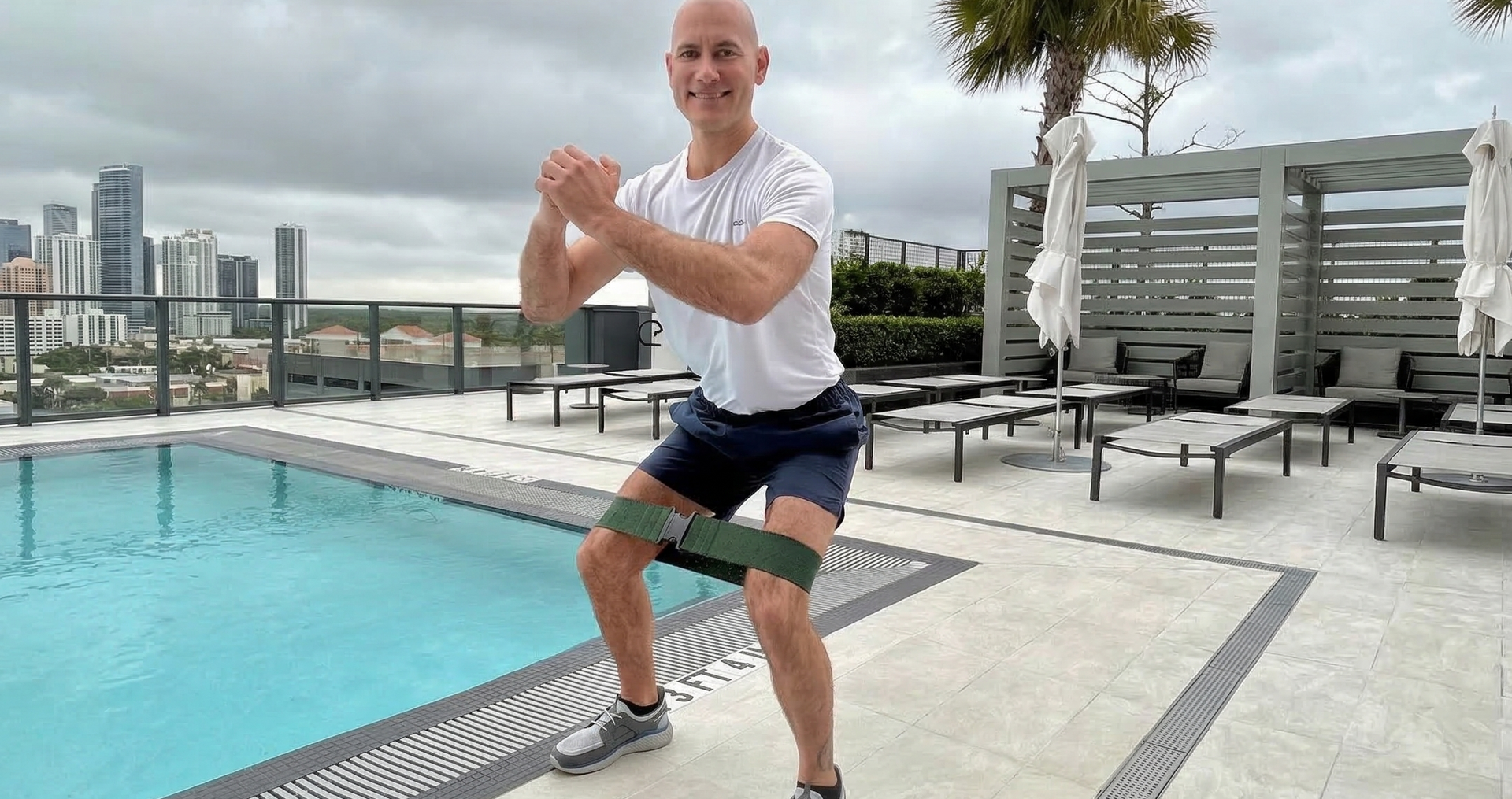 Man exercising with his Booya Band glute booty resistance band by a pool with a city skyline in the background